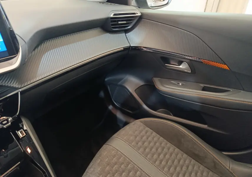 Intérieur côté passager du Peugeot 208 Electrique Roadtrip 2022, avec garnitures noires et surpiqûres orange.