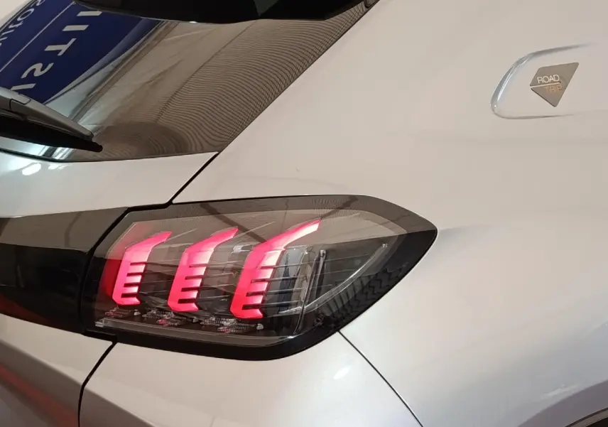 Gros plan sur le feu arrière droit allumé d’une Peugeot 208 Electrique ROADTRIP gris clair, avec badge spécifique visible.