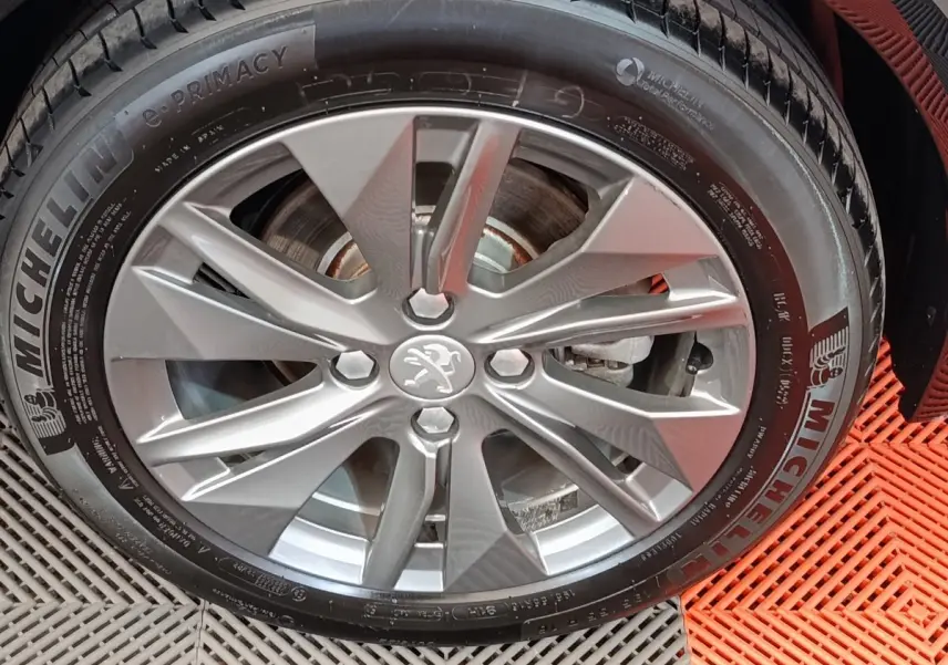 Vue de profil côté gauche d'une Peugeot 208 électrique Roadtrip gris clair sur sol rouge avec roue avant visible.