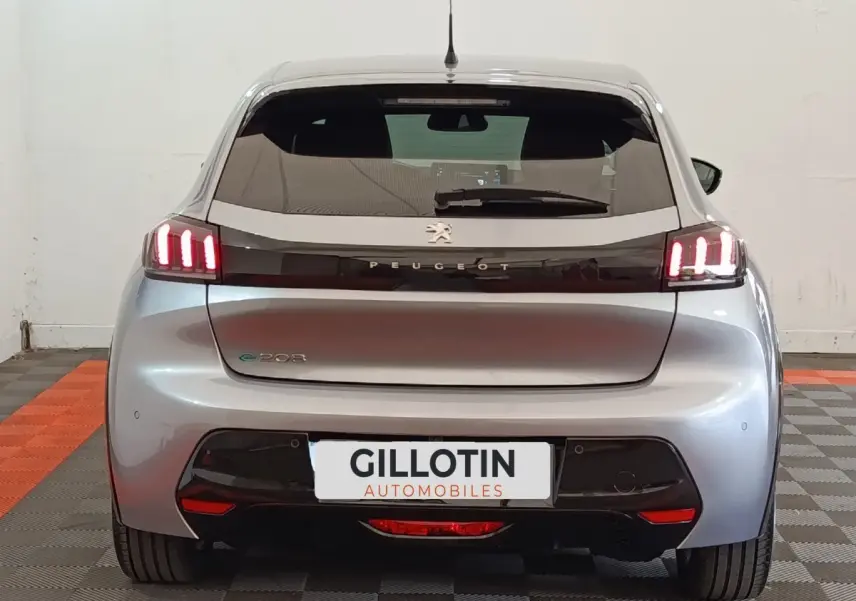 Vue arrière de la Peugeot 208 électrique gris clair avec feux LED distinctifs et logo Peugeot lumineux.