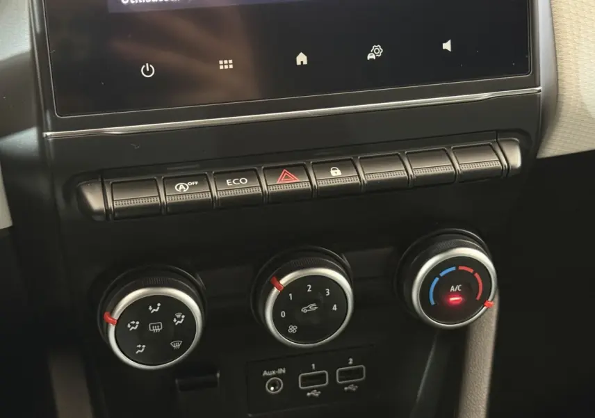 Gros plan sur la console centrale de la Renault Clio blanche 2023, montrant les commandes de climatisation et boutons fonctionnels.