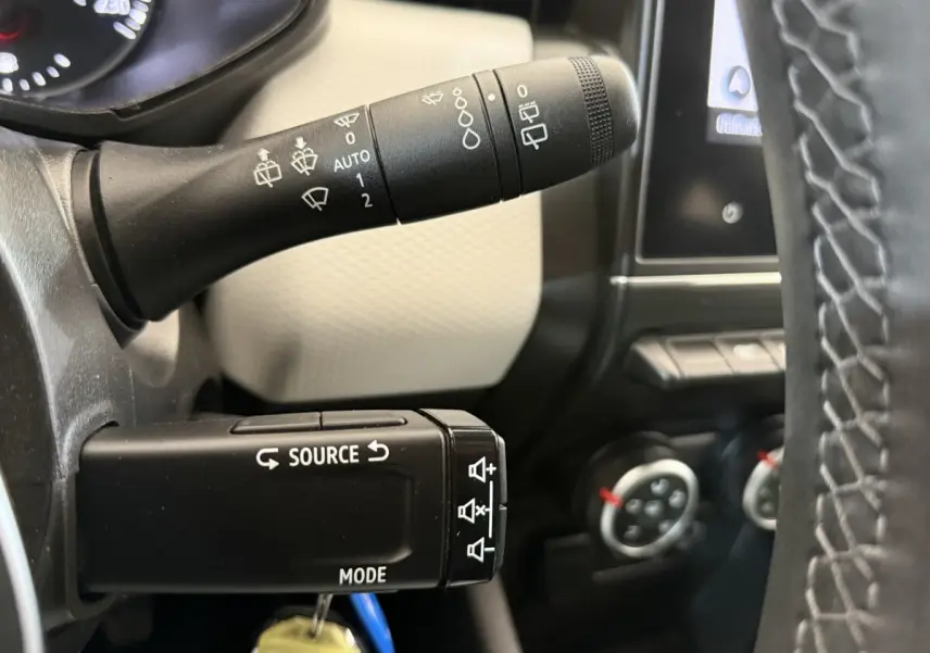 Gros plan sur les commandes au volant noir de la Renault Clio 2023, avec tableau de bord et écran tactile en arrière-plan.