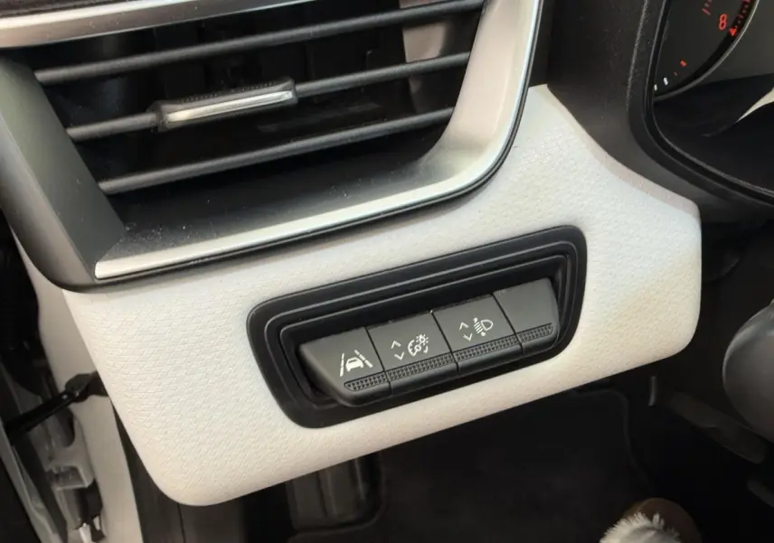 Gros plan sur les commandes d'assistance à la conduite sous la grille d'aération, intérieur blanc de la Renault Clio Evolution TCe 100 GPL.