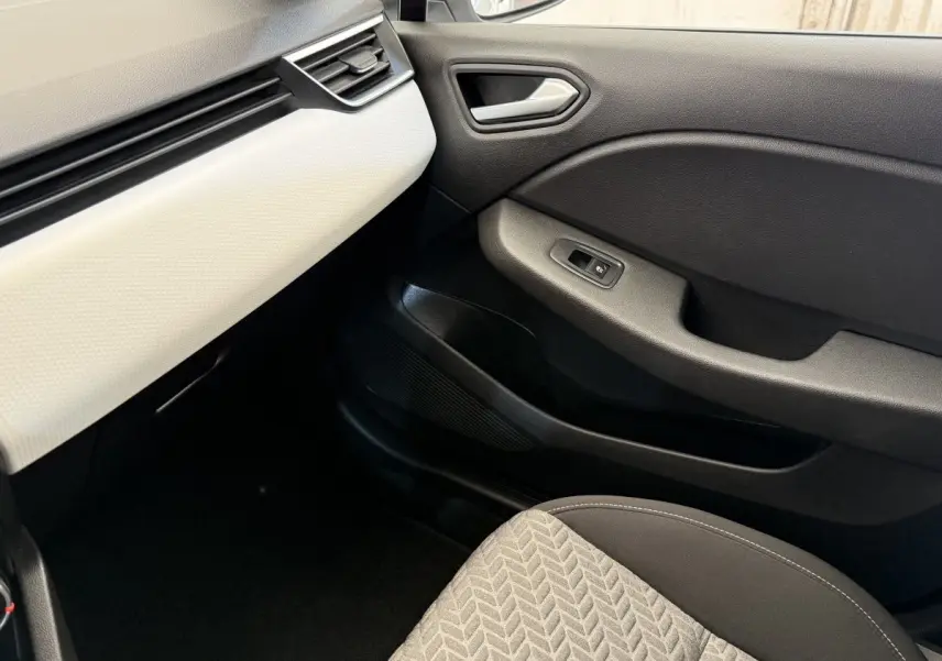 Intérieur côté passager de la Renault Clio blanc avec tableau de bord clair et porte noire, siège tissu gris à motifs.