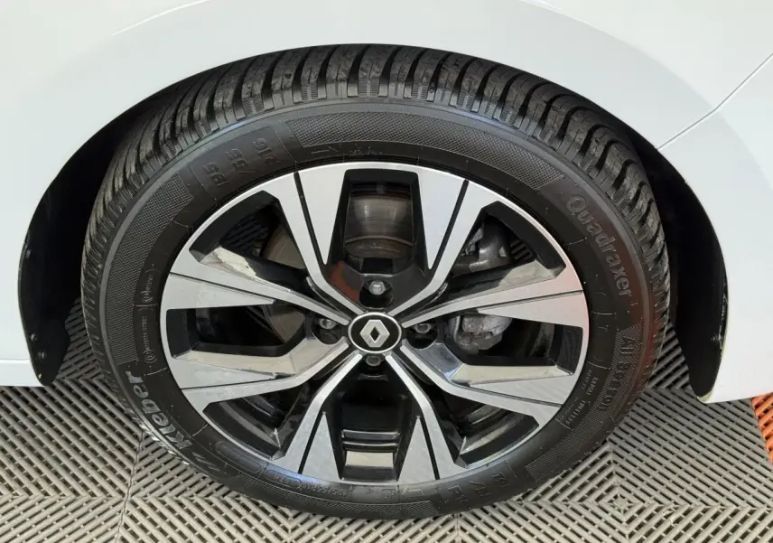 Gros plan sur la roue avant droite d'une Renault Clio blanche, mettant en valeur la jante alliage au design moderne.