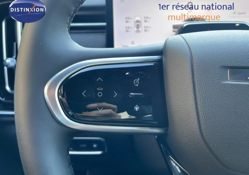 Gros plan sur les commandes tactiles au volant côté gauche du JAECOO J7 noir carbone, avec tableau de bord numérique en arrière-plan.