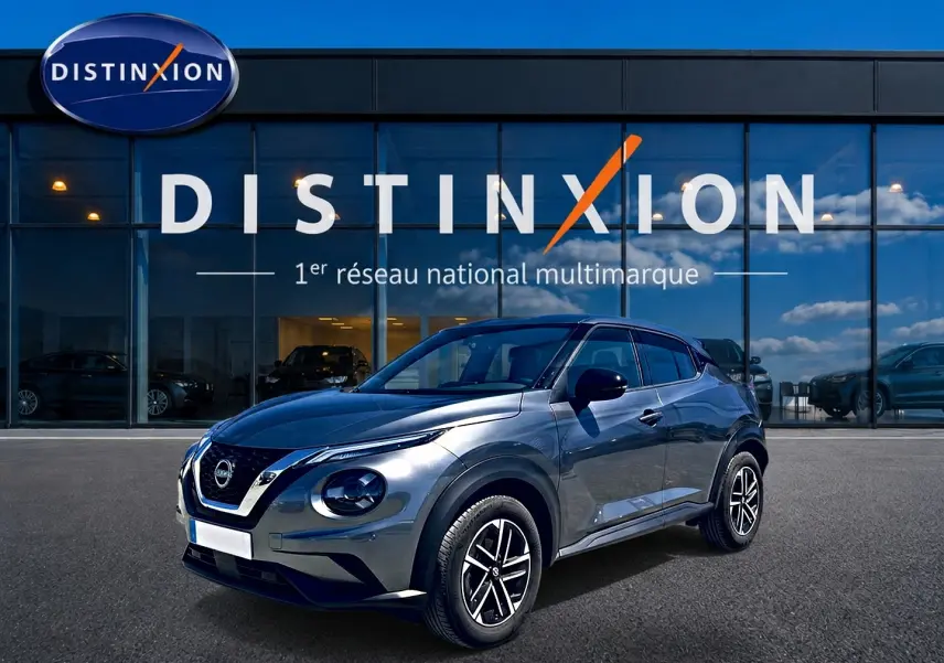 Nissan Juke gris 3/4 avant droit avec jantes alu, garé devant une vitrine Distinxion.