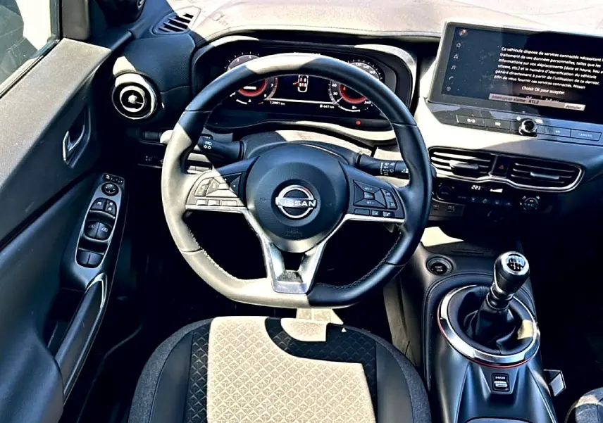 Vue intérieure centrée sur le volant cuir multifonction et levier de vitesse manuel du Nissan Juke gris 2025.