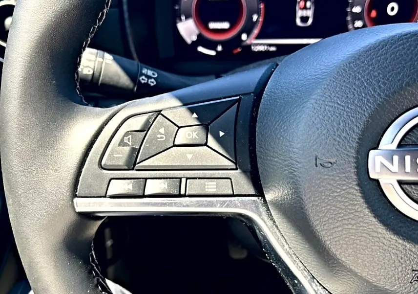 Gros plan sur les commandes multifonctions à gauche du volant cuir noir du Nissan Juke gris 2025, tableau de bord en arrière-plan.
