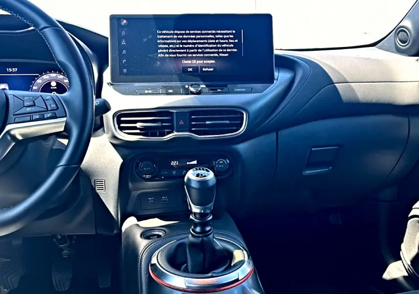 Intérieur du Nissan Juke 2025 vu de face, volant cuir à gauche, écran tactile central et levier de vitesse manuel.