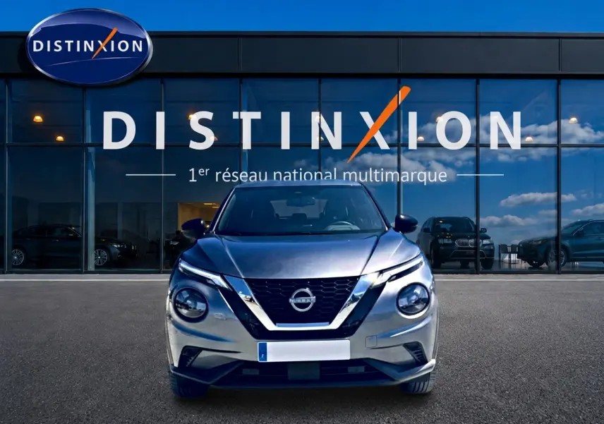 Vue avant d'un Nissan Juke gris 2025 avec calandre en V chromée, phares ronds et logo Nissan visible.