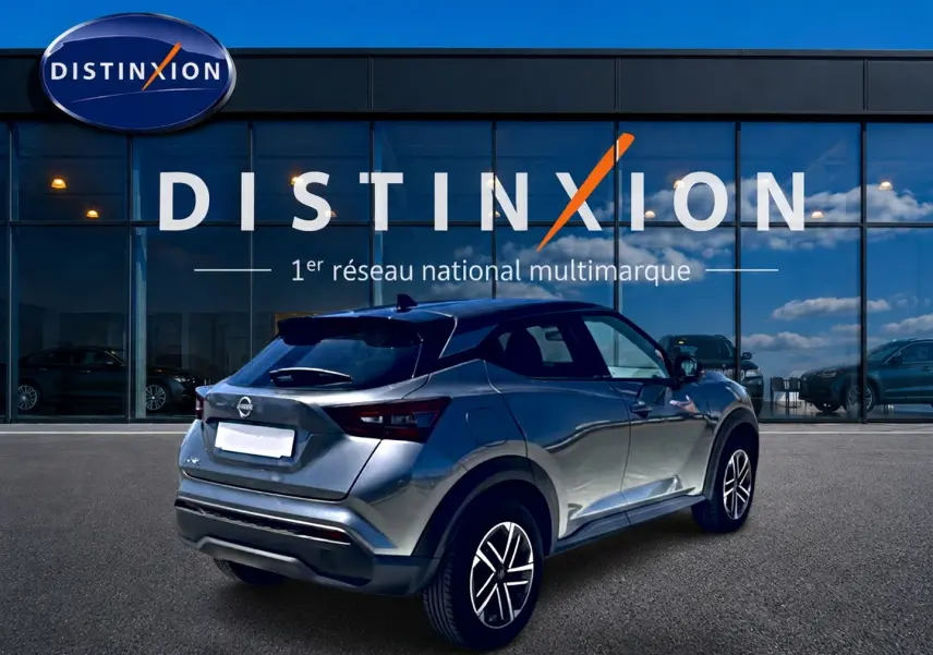 Nissan Juke gris 3/4 arrière droit, avec jantes alu et toit noir, devant une vitrine Distinxion.