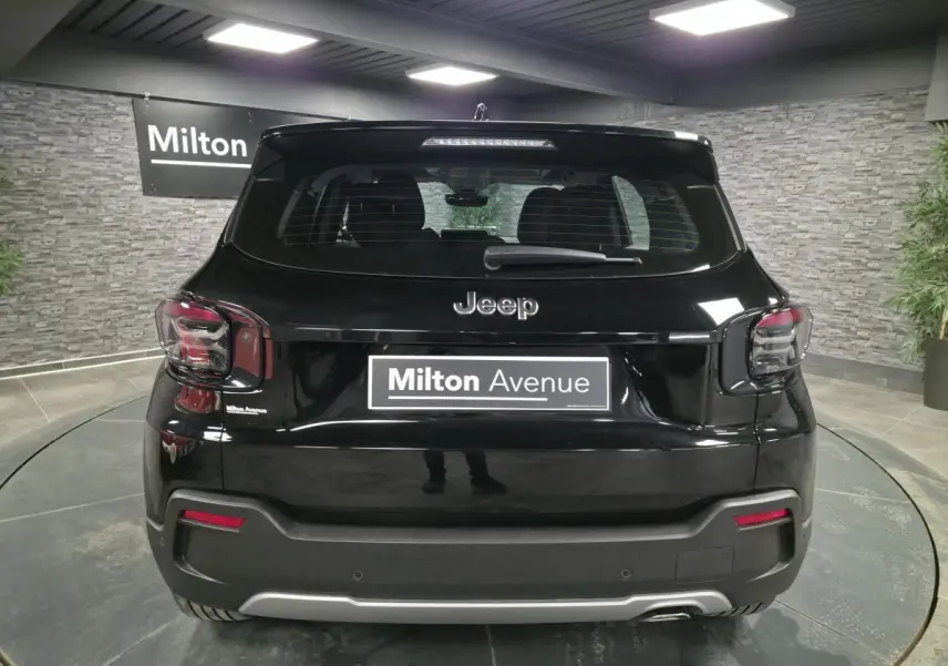 Vue arrière d'un Jeep Avenger noir avec feux arrière fumés et plaque Milton Avenue dans un showroom.