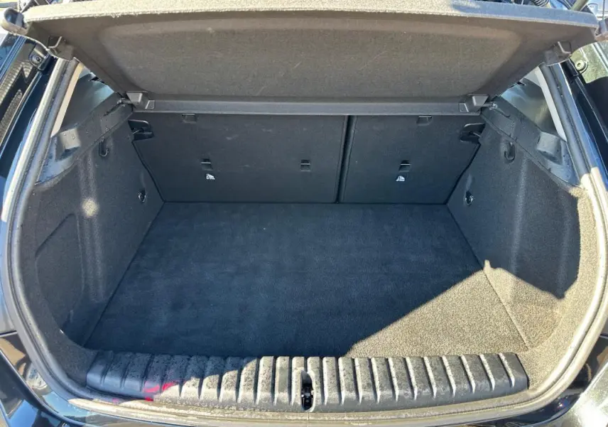 Coffre ouvert vu de l'arrière d'une BMW Série 1 F40 118d noire, espace de chargement propre et vide.