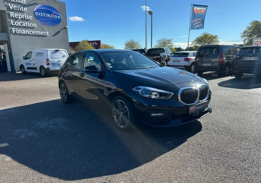 BMW Série 1 F40 118d noire vue 3/4 avant droit sur parking ensoleillé devant un garage Distinxion.