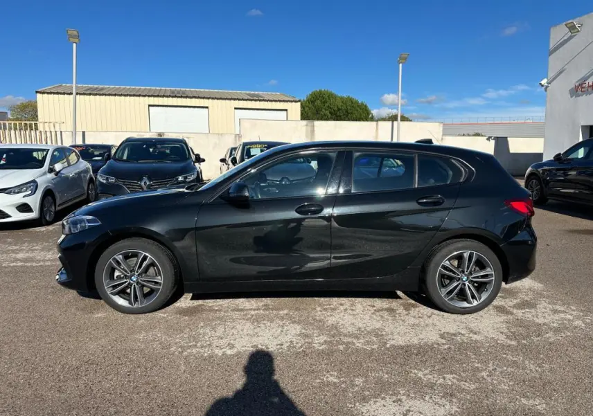 Profil côté gauche d'une BMW Série 1 F40 noire, avec jantes alliage 17 pouces, stationnée en extérieur au soleil.