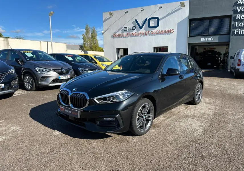 BMW Série 1 F40 118d noire vue en 3/4 avant droit sur parking devant concession Sud VO.