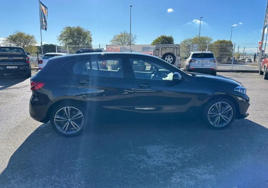 BMW Série 1 F40 118d noire vue de profil côté gauche, avec jantes alliage 17 pouces et toit ouvrant panoramique.