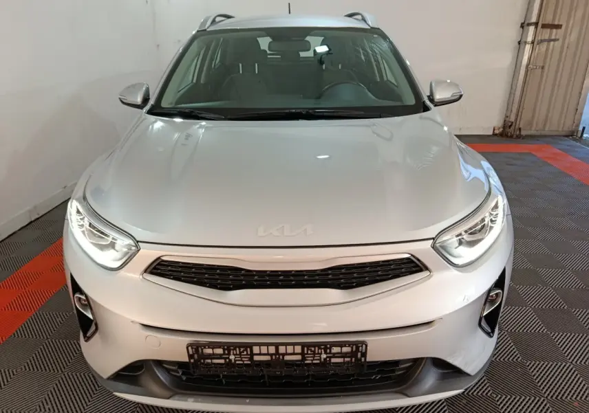 Vue avant d'un KIA Stonic gris clair 2022 avec phares allumés et calandre noire dans un garage.