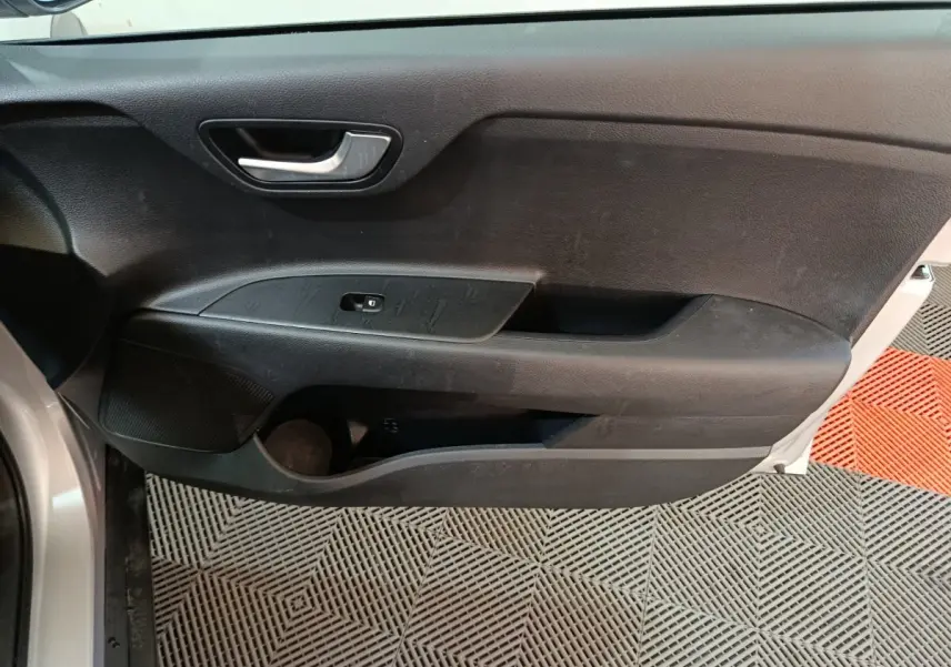 Vue rapprochée de la porte avant gauche noire d’une KIA Stonic gris clair, avec poignée argentée et commande de vitre.