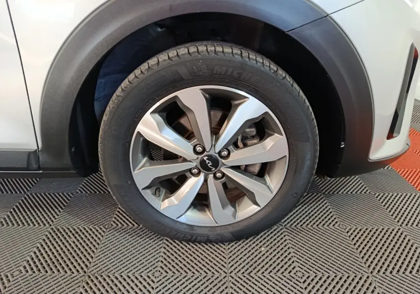 Gros plan sur la roue avant droite d'un KIA Stonic gris clair, avec jante alliage et logo KIA visible au centre.