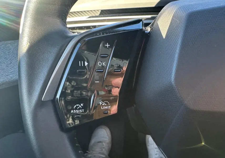 Gros plan sur les commandes noires au volant du Peugeot 3008 Hybrid blanc, avec boutons de réglage et assistance.