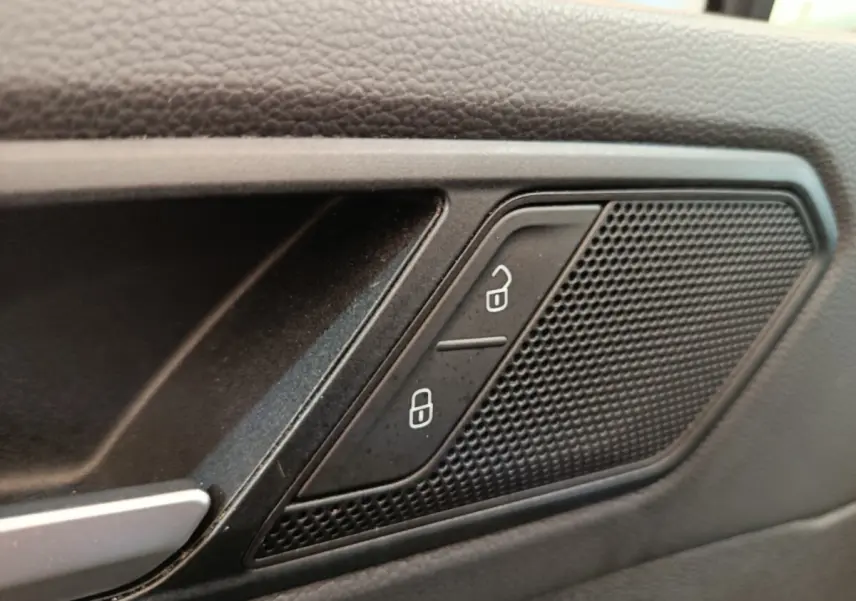 Gros plan sur la commande de verrouillage des portes et haut-parleur intégré dans la porte intérieure noire du Volkswagen Tiguan.