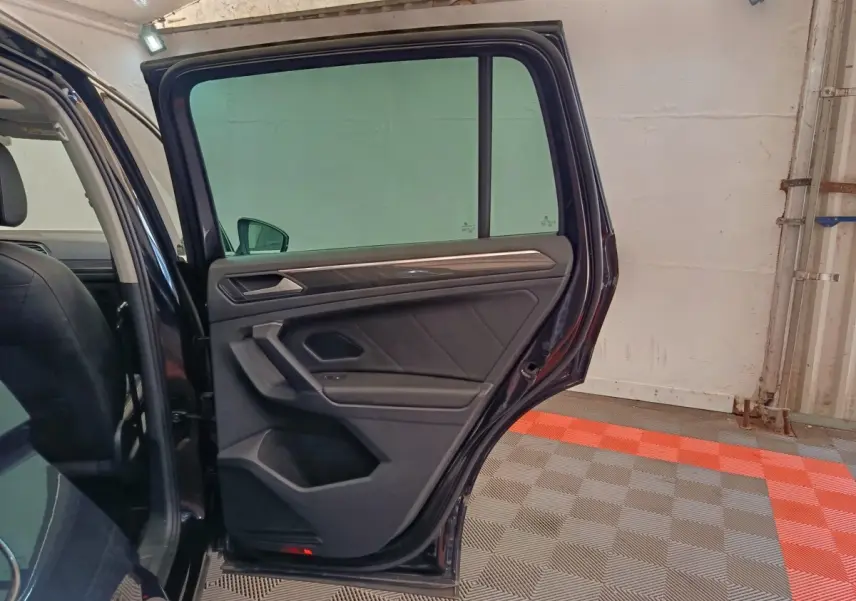 Vue intérieure côté arrière gauche du Volkswagen Tiguan noir 2022, porte ouverte avec garniture et poignée visibles.