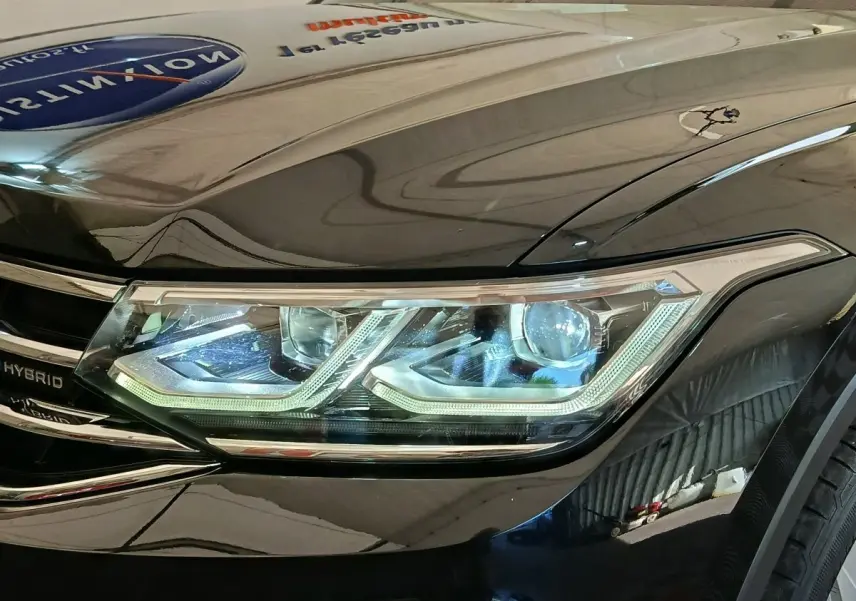 Gros plan sur le phare avant droit LED du Volkswagen Tiguan noir, mettant en valeur les détails lumineux et la calandre hybride.