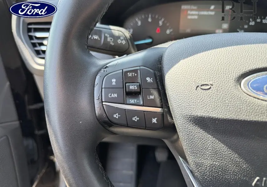Gros plan sur le volant cuir multifonction noir de la Ford Focus 1.0 Flexifuel, avec commandes de régulateur et volume visibles.