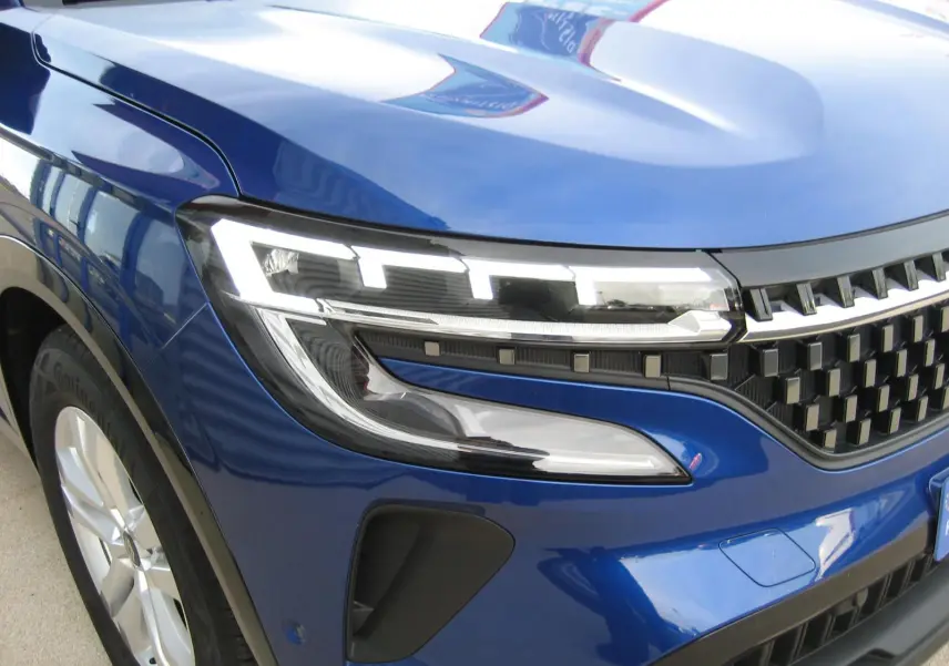 Gros plan sur l'avant droit du Renault Austral bleu Iron, mettant en valeur le phare LED et la calandre noire.
