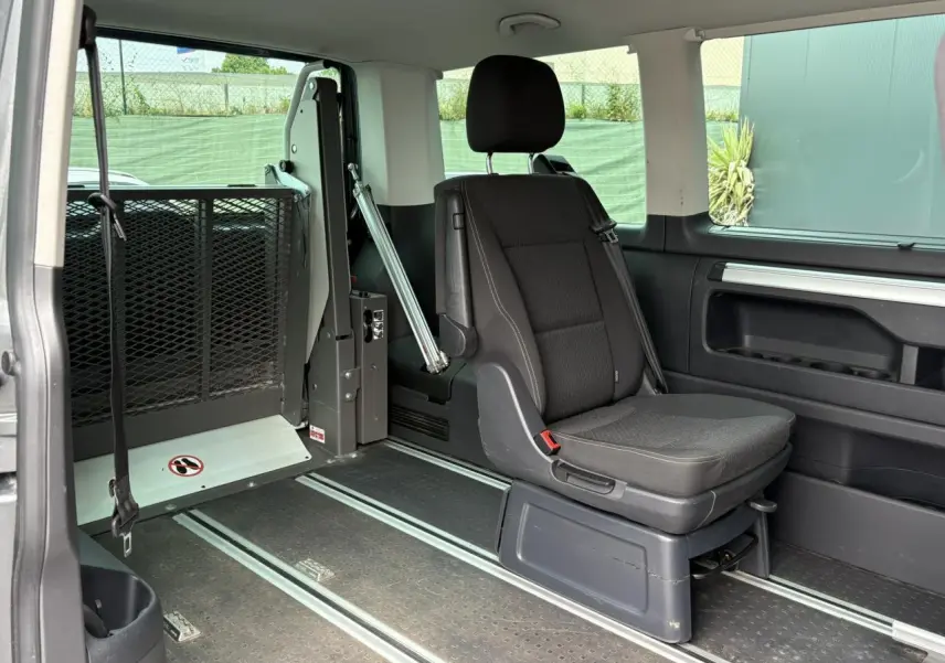 Siège passager noir et aménagement TPMR visibles à l'intérieur d'un Volkswagen Multivan gris Indium, vue latérale droite.