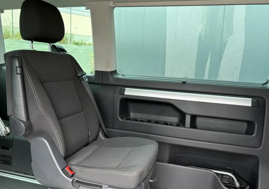 Siège passager arrière noir du Volkswagen Multivan T6 2019 avec porte coulissante droite et fenêtre teintée.