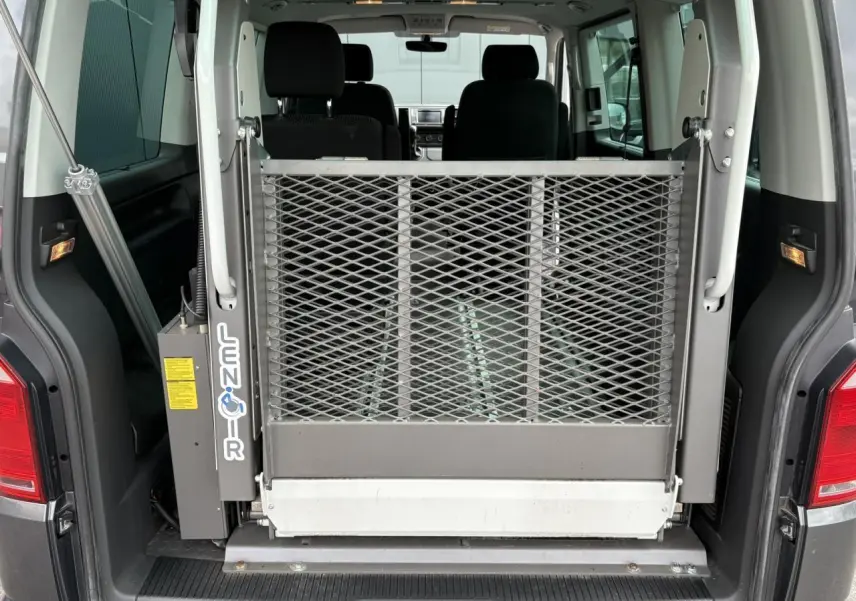 Vue arrière ouverte du Volkswagen Multivan T6 gris Indium avec rampe d'accès TPMR déployée dans le coffre.