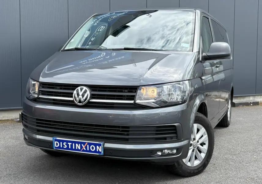 Volkswagen Multivan T6 gris Indium vu en 3/4 avant droit avec phares allumés et jantes alliage.
