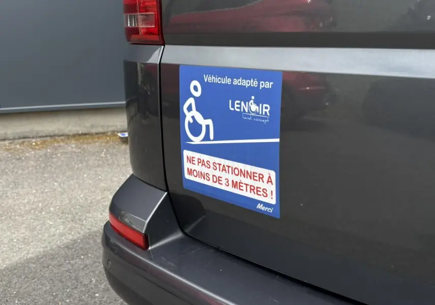Vue arrière gauche du Volkswagen Multivan gris Indium avec autocollant handicap et message de stationnement interdit.