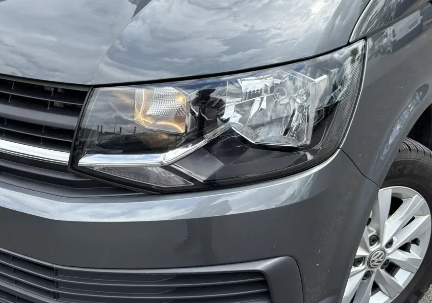 Gros plan sur le phare avant droit et la calandre d'un Volkswagen Multivan gris Indium avec jante alliage visible.