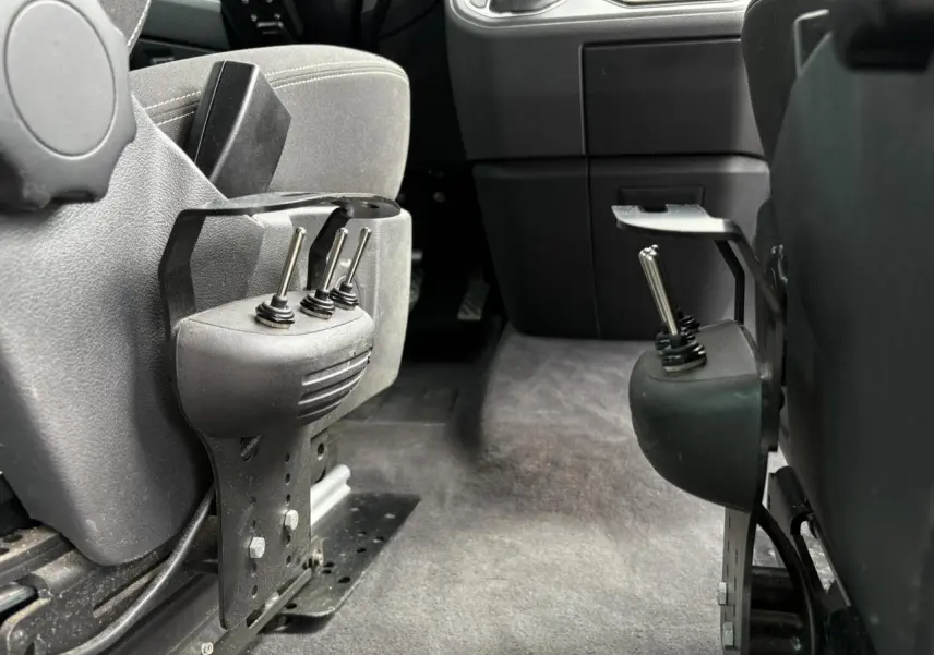 Gros plan sur les commandes manuelles d'accessibilité entre les sièges avant du Volkswagen Multivan T6 gris Indium.