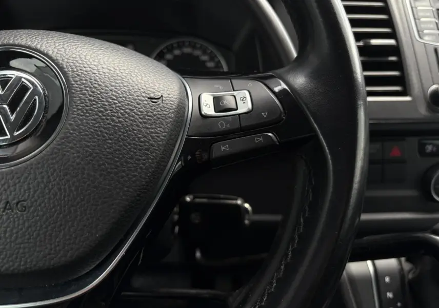 Gros plan sur le volant cuir multifonction noir du Volkswagen Multivan T6 avec commandes intégrées et tableau de bord partiel.