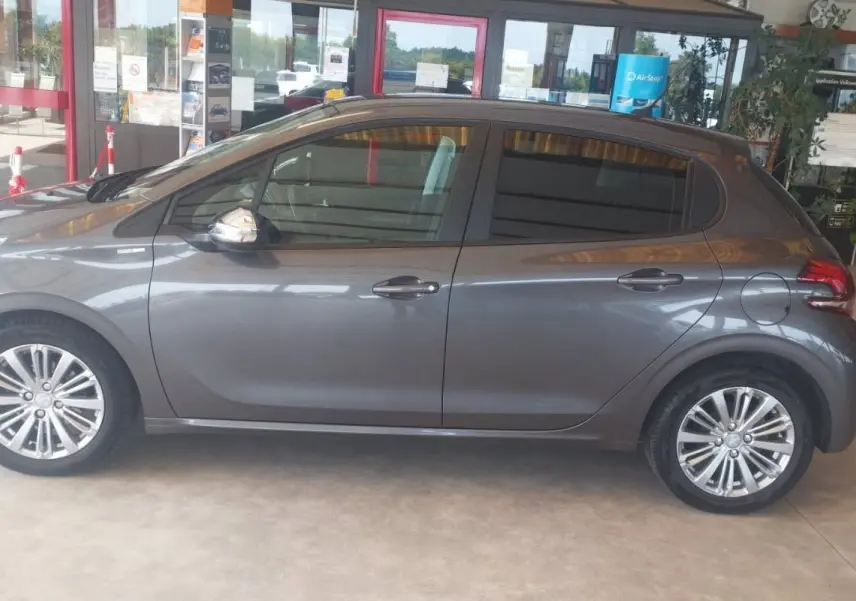 Profil côté gauche d'une Peugeot 208 gris métal 2023, compacte et élégante, en intérieur de showroom lumineux.