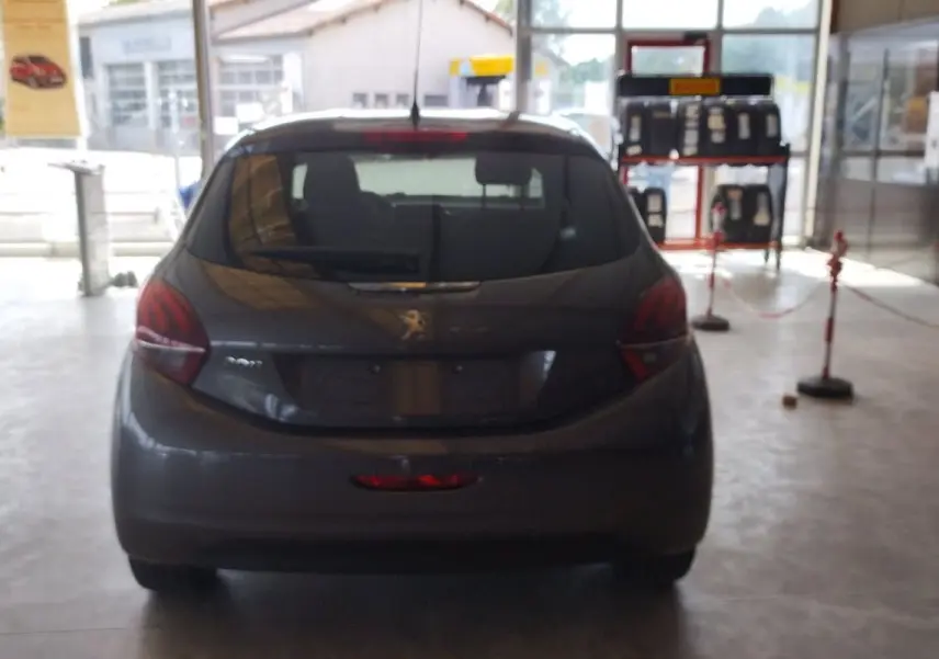 Vue arrière d'une Peugeot 208 gris métal 2023 en showroom, mettant en valeur ses feux arrière et sa silhouette compacte.
