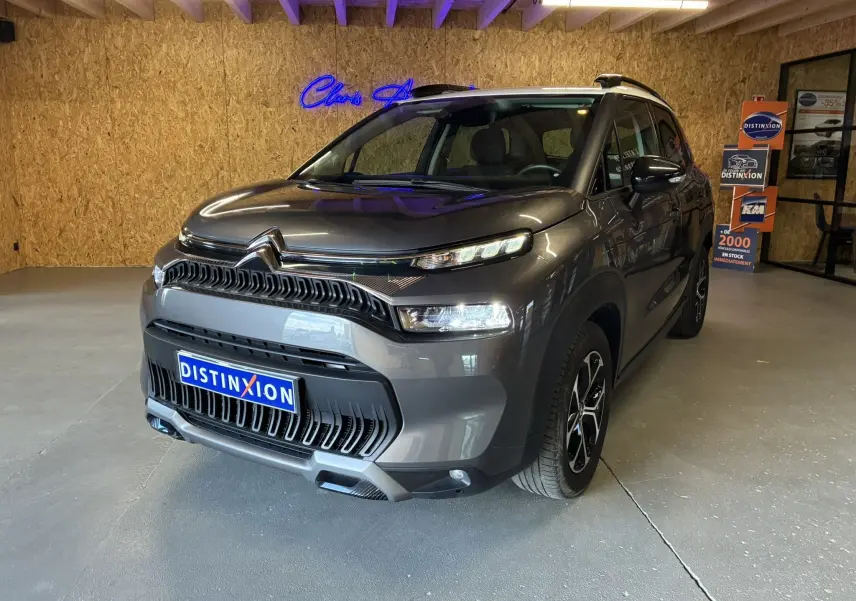 Citroën C3 Aircross gris platinium métal vue 3/4 avant droit avec toit blanc et jantes bi-ton en intérieur showroom.