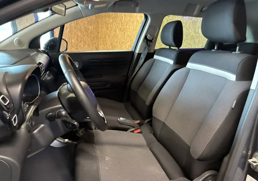 Vue intérieure côté conducteur du Citroën C3 Aircross 2023 avec sièges tissu gris noir et volant cuir multifonction.
