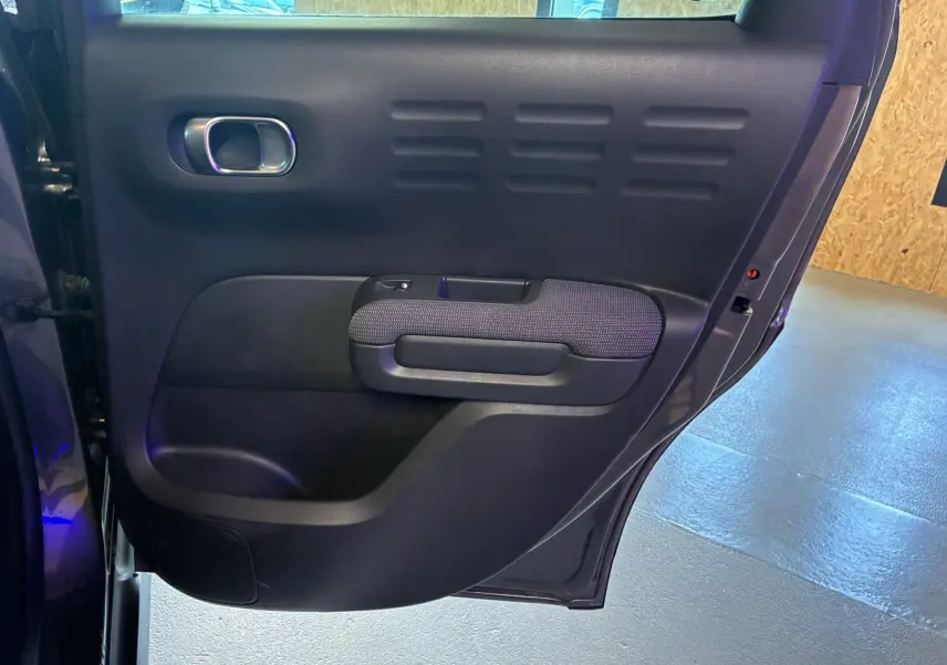 Porte arrière gauche ouverte du Citroën C3 Aircross 2023 gris platinium, tissu gris noir et poignée chromée visible.