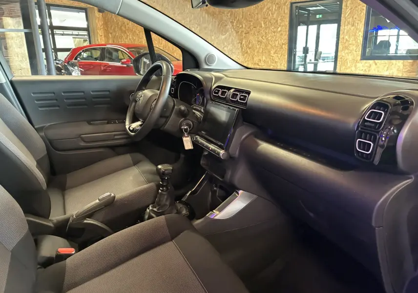 Vue intérieure côté conducteur de la Citroën C3 Aircross 2023 avec sièges tissu gris et tableau de bord noir moderne.