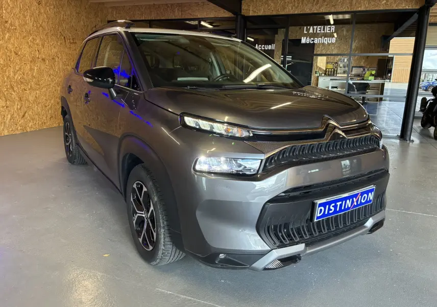 Citroën C3 Aircross gris platinium en 3/4 avant droit, avec toit blanc et jantes bi-ton, stationné en intérieur.