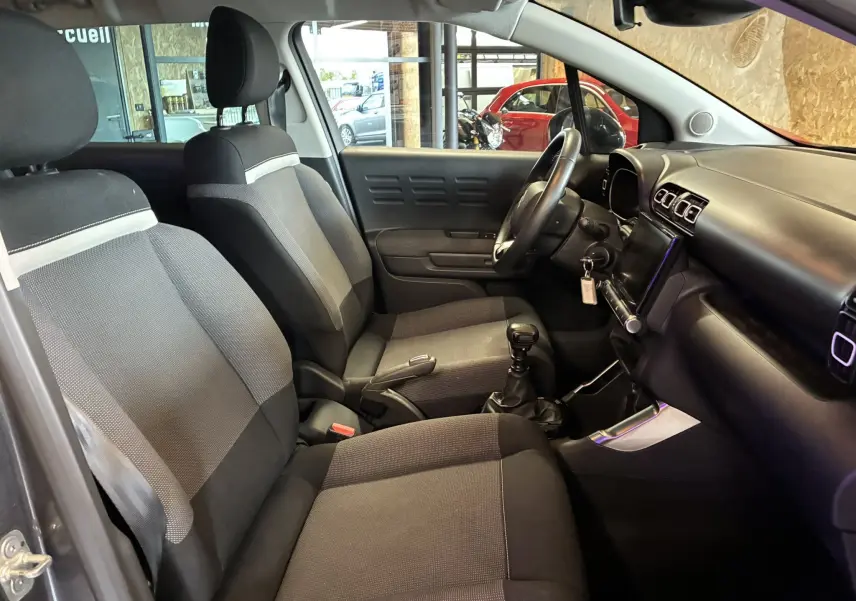 Intérieur côté conducteur du Citroën C3 Aircross 2023, sièges tissu gris noir et tableau de bord avec écran tactile.
