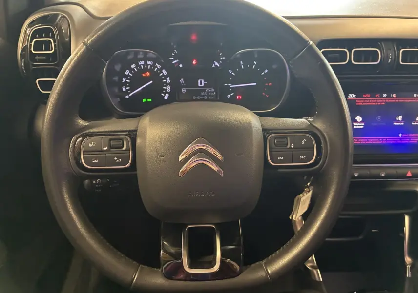 Vue rapprochée du volant en cuir noir multifonction d'une Citroën C3 Aircross 2023 avec tableau de bord et écran tactile visible.