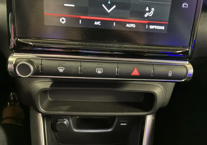 Gros plan sur la console centrale du Citroën C3 Aircross 2023, boutons de climatisation et rangement noir mat.