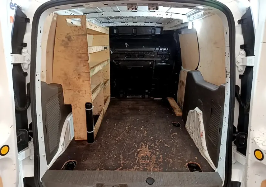 Vue arrière du fourgon Ford Transit blanc 2022, montrant l’intérieur utilitaire avec étagères en bois à gauche.